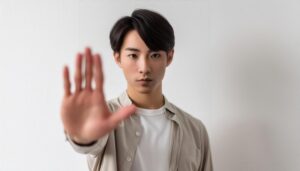 白背景でNOのジェスチャーをする若い男性（ライトシャツ）