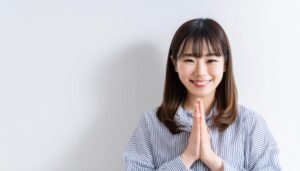 白背景で祈りのポーズをとる若い女性（ストライプシャツ）