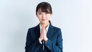 白背景で祈りのポーズをとる若い女性（スーツ）