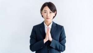 白背景で手を合わせる若い女性（スーツ）