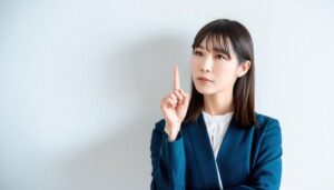 白背景で人差し指を立てる若い女性（スーツ）