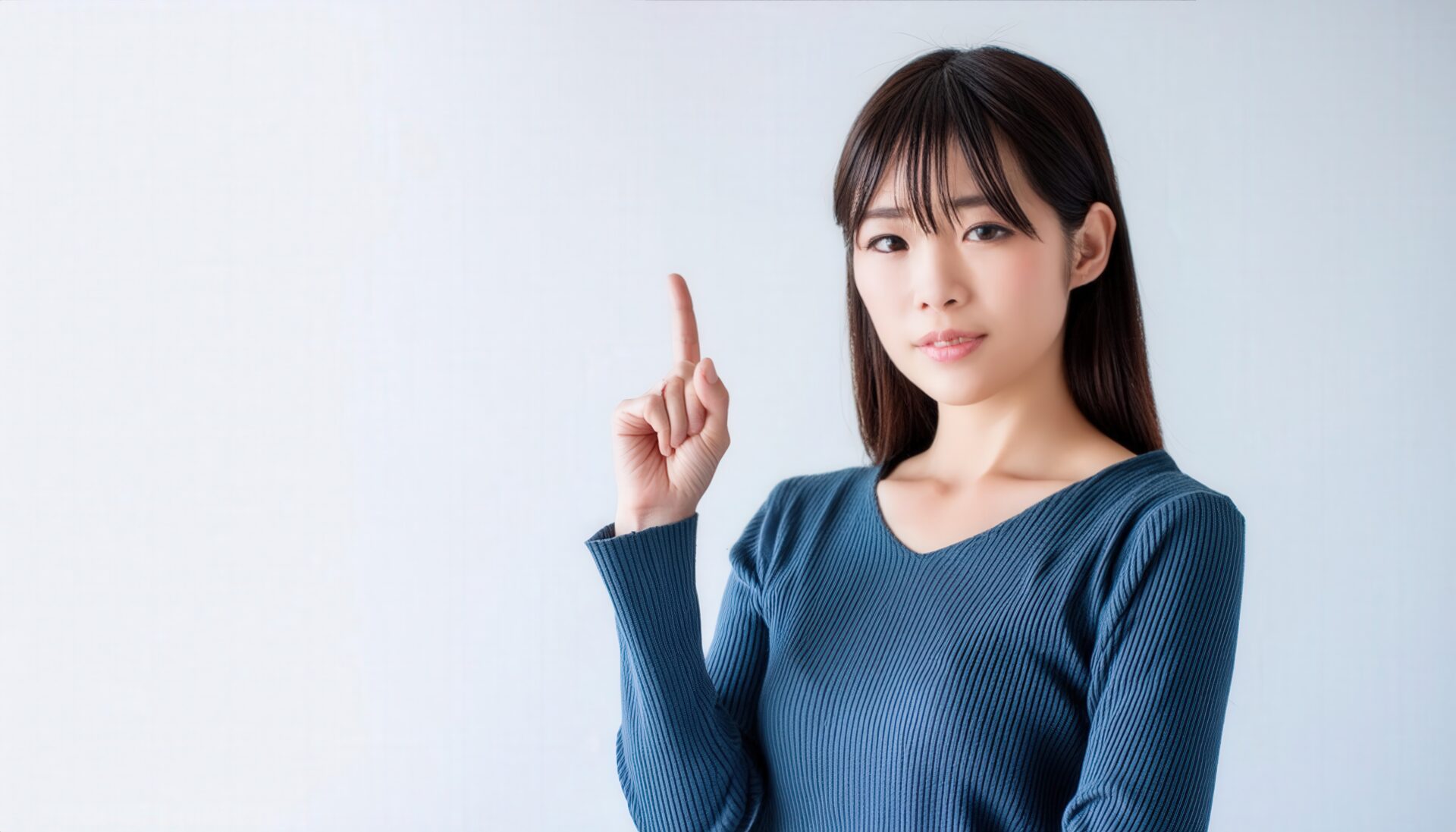 白背景で人差し指を立てる若い女性（カジュアル）
