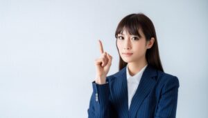 白背景で人差し指を立てる若い女性（ピンストライプスーツ）