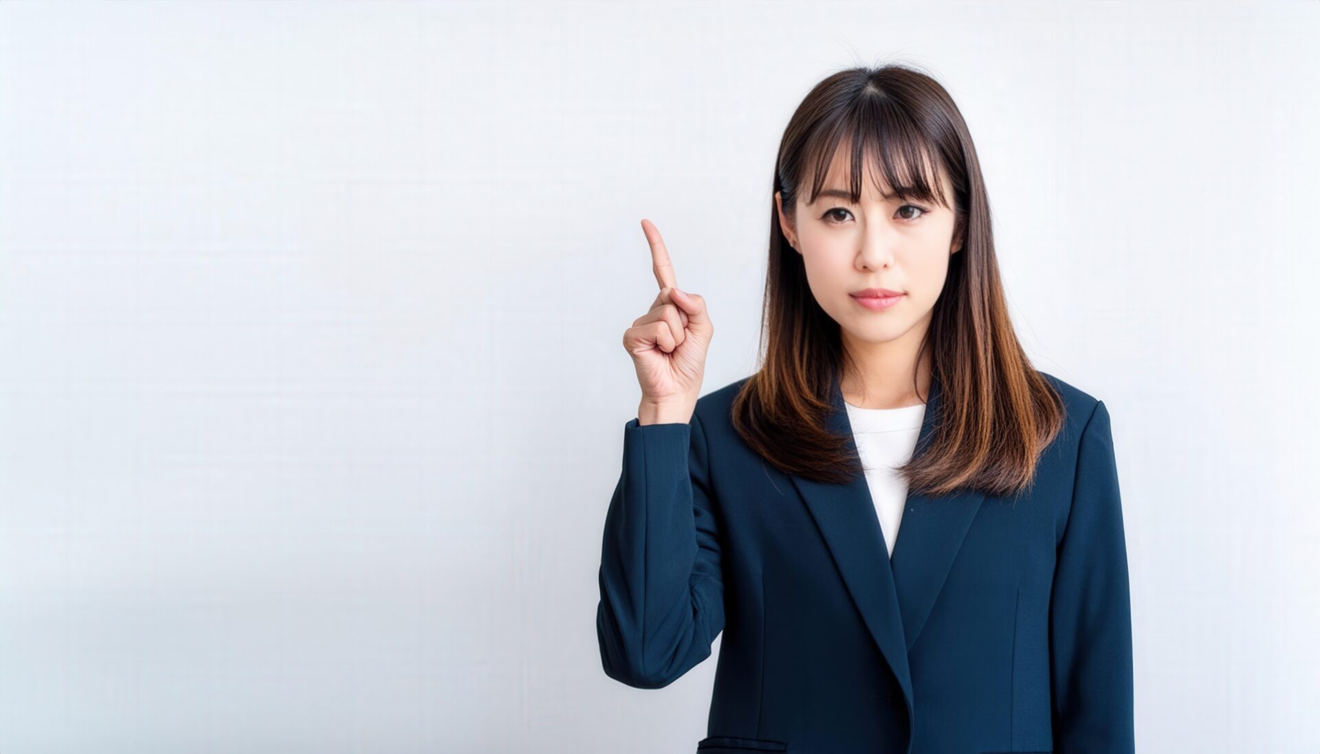 白背景で人差し指を立てる若い女性（スーツ）