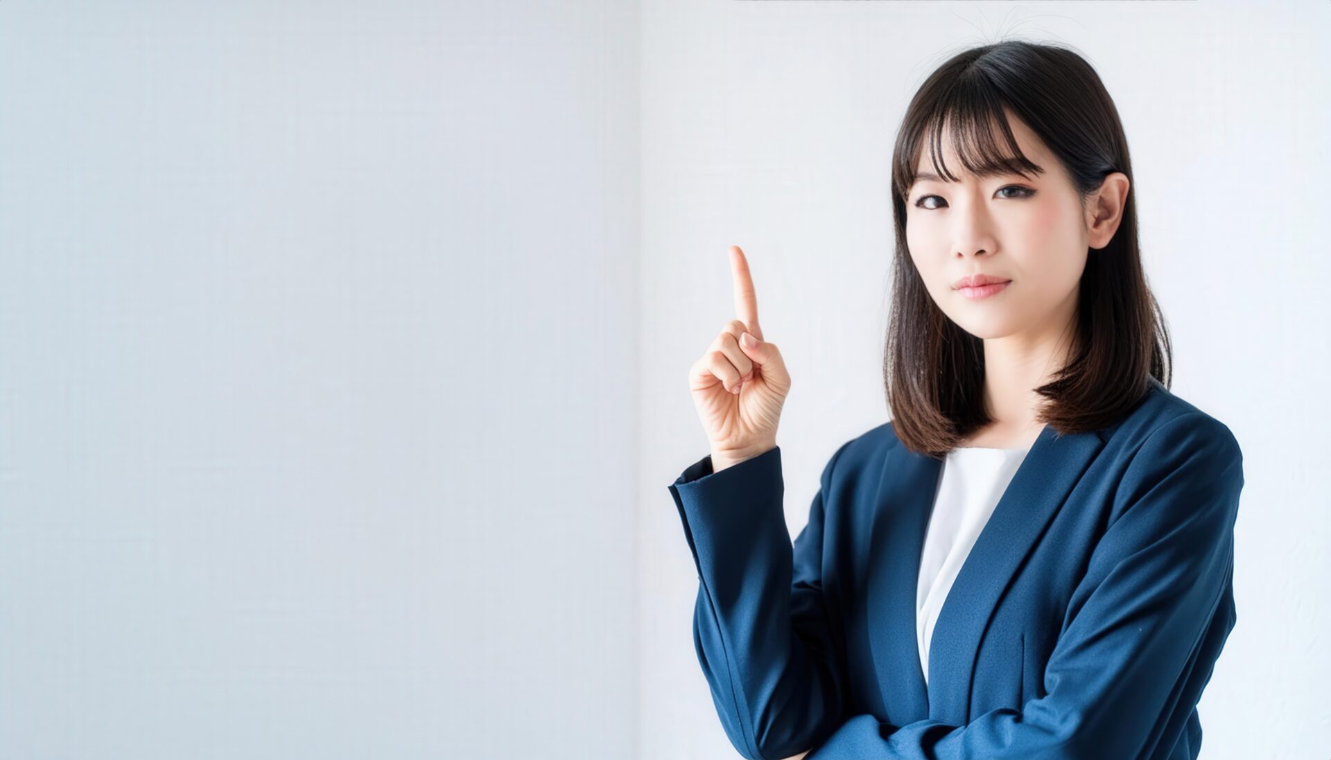 白背景で人差し指を立てる若い女性（スーツ）