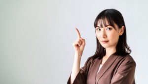 白背景で人差し指を立てる若い女性（ブラウンジャケット）