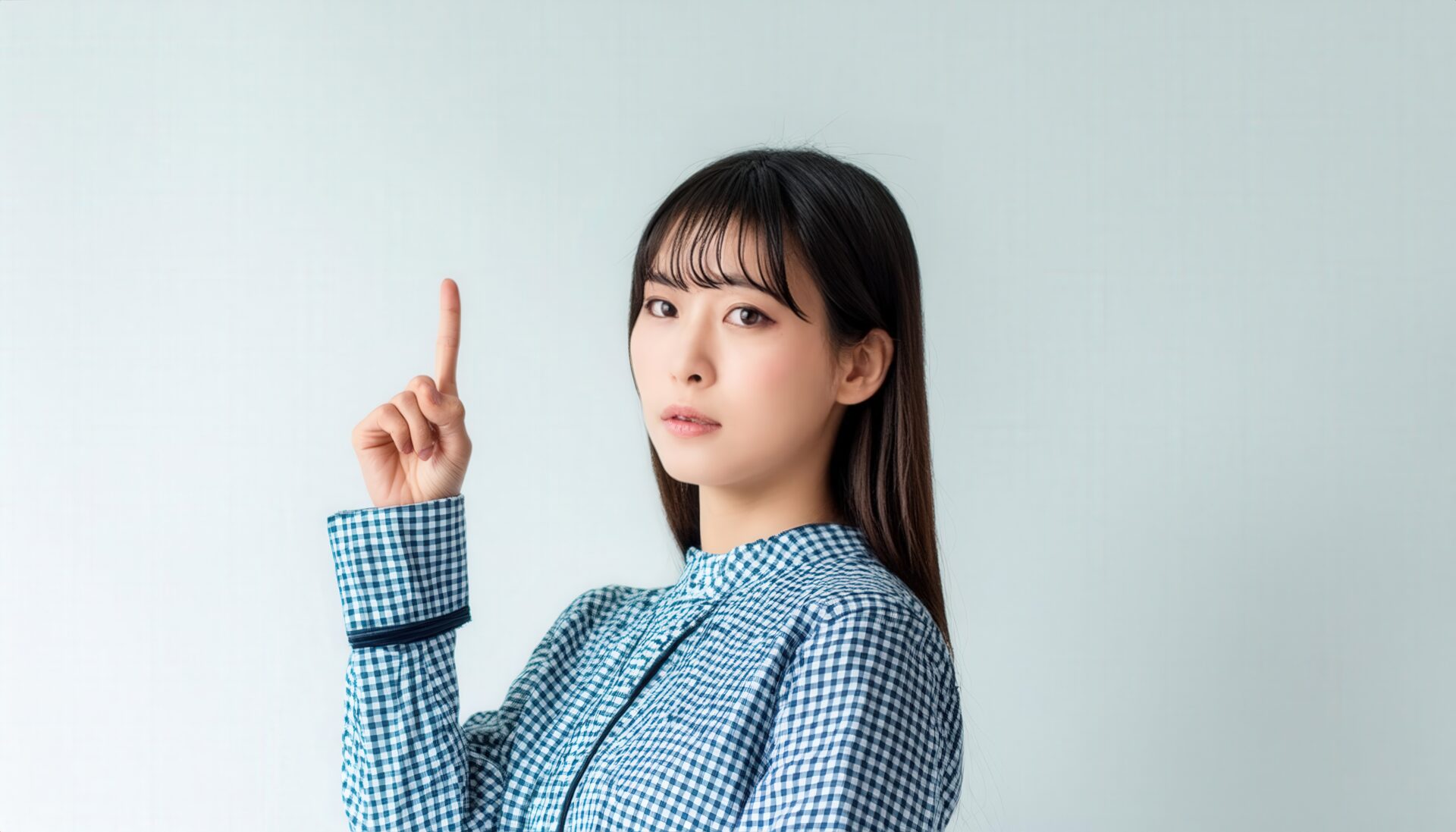 白背景で人差し指を立てる若い女性（チェック柄シャツ）