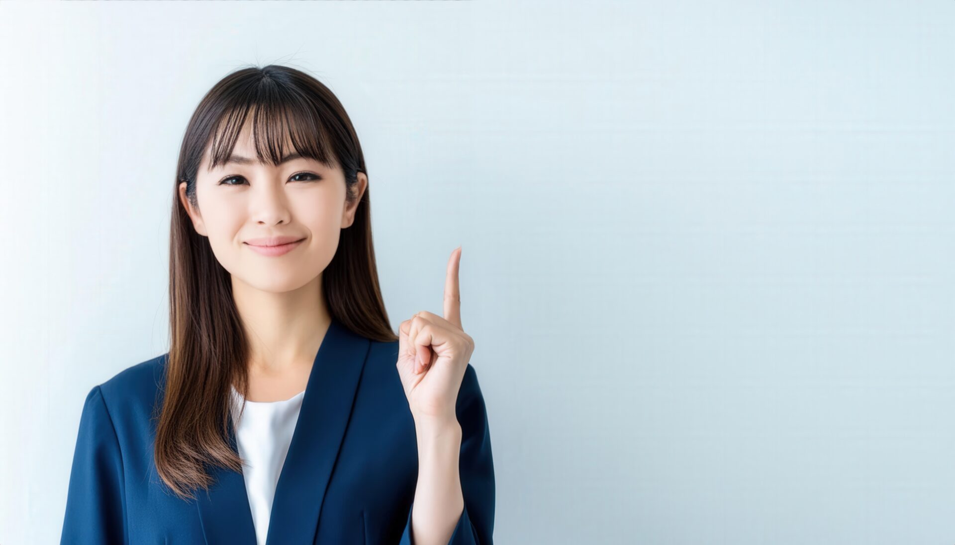 白背景で人差し指を立てる若い女性（スーツ）