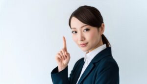 白背景で人差し指を立てる若い女性（スーツ・ポニーテール）