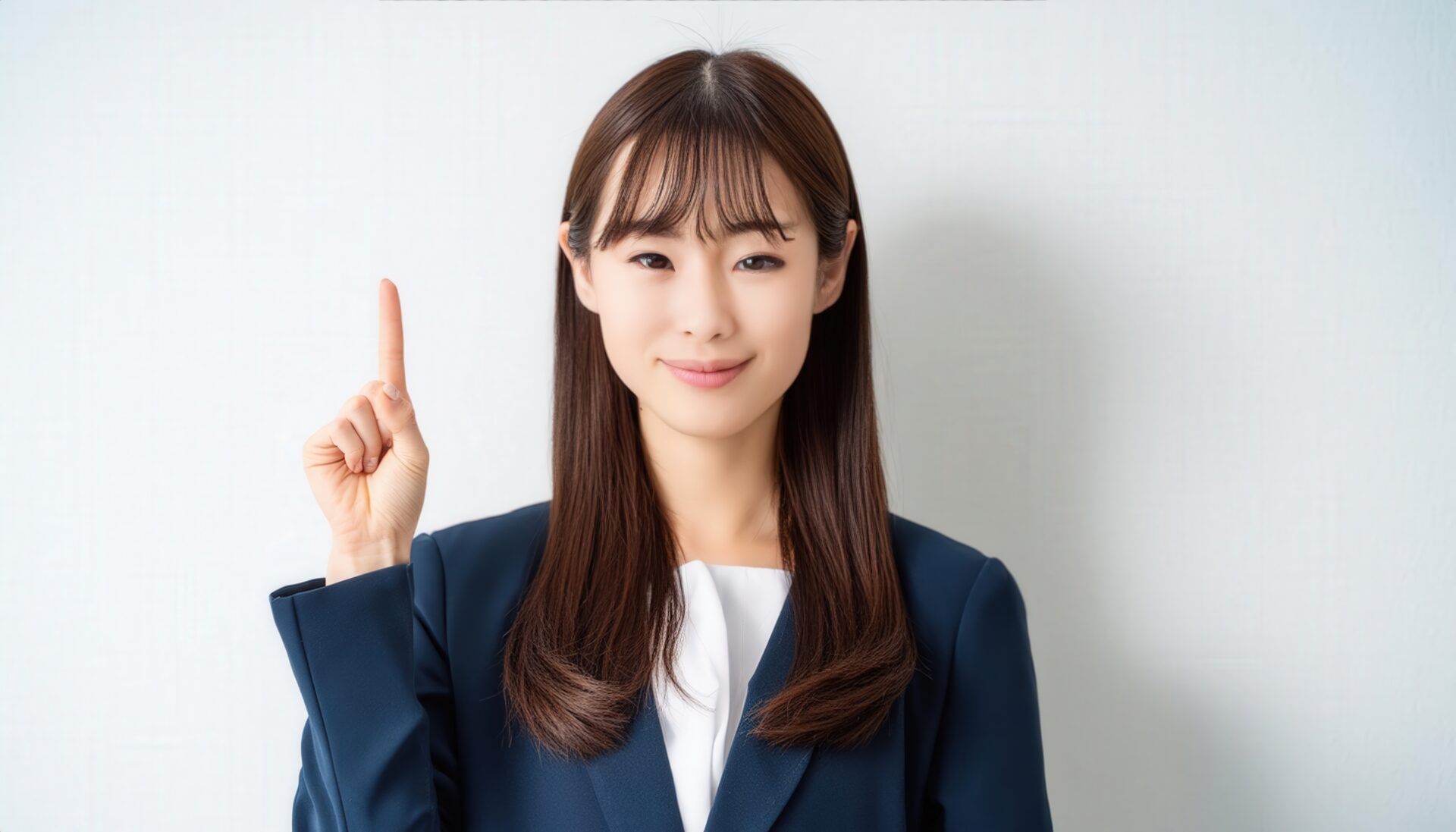 白背景で人差し指を立てる若い女性（スーツ・ロングヘア）
