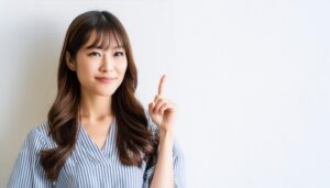 白背景で人差し指を立てる若い女性（ストライプトップス）