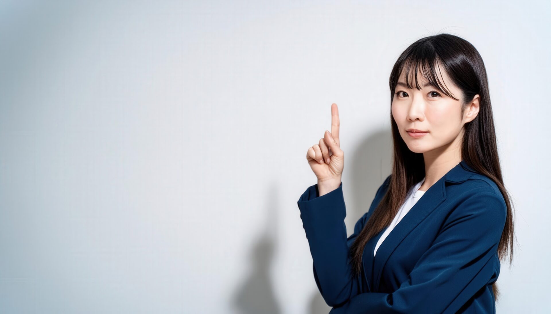 白背景で人差し指を立てる若い女性（スーツ）