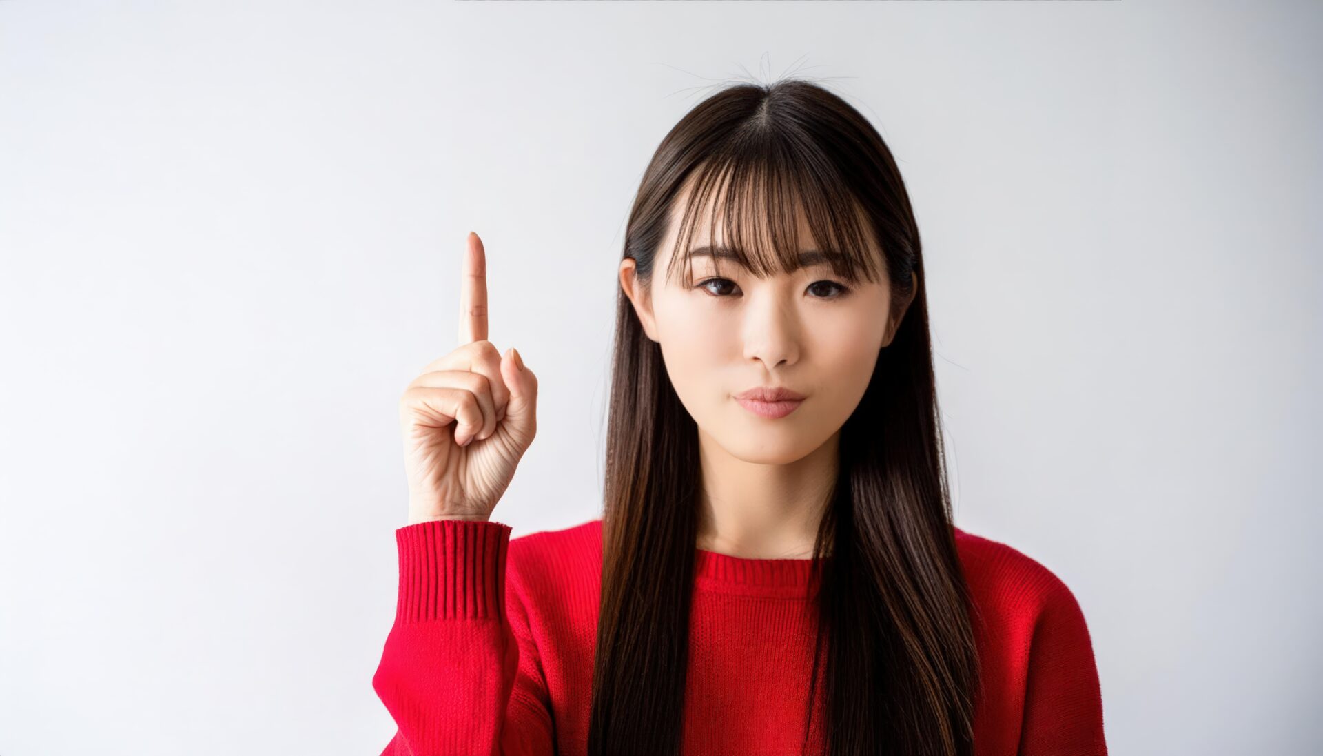 白背景で人差し指を立てる若い女性（赤いセーター）