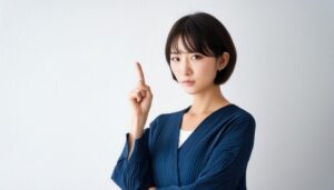 白背景で人差し指を立てる若い女性（ネイビーブラウス）