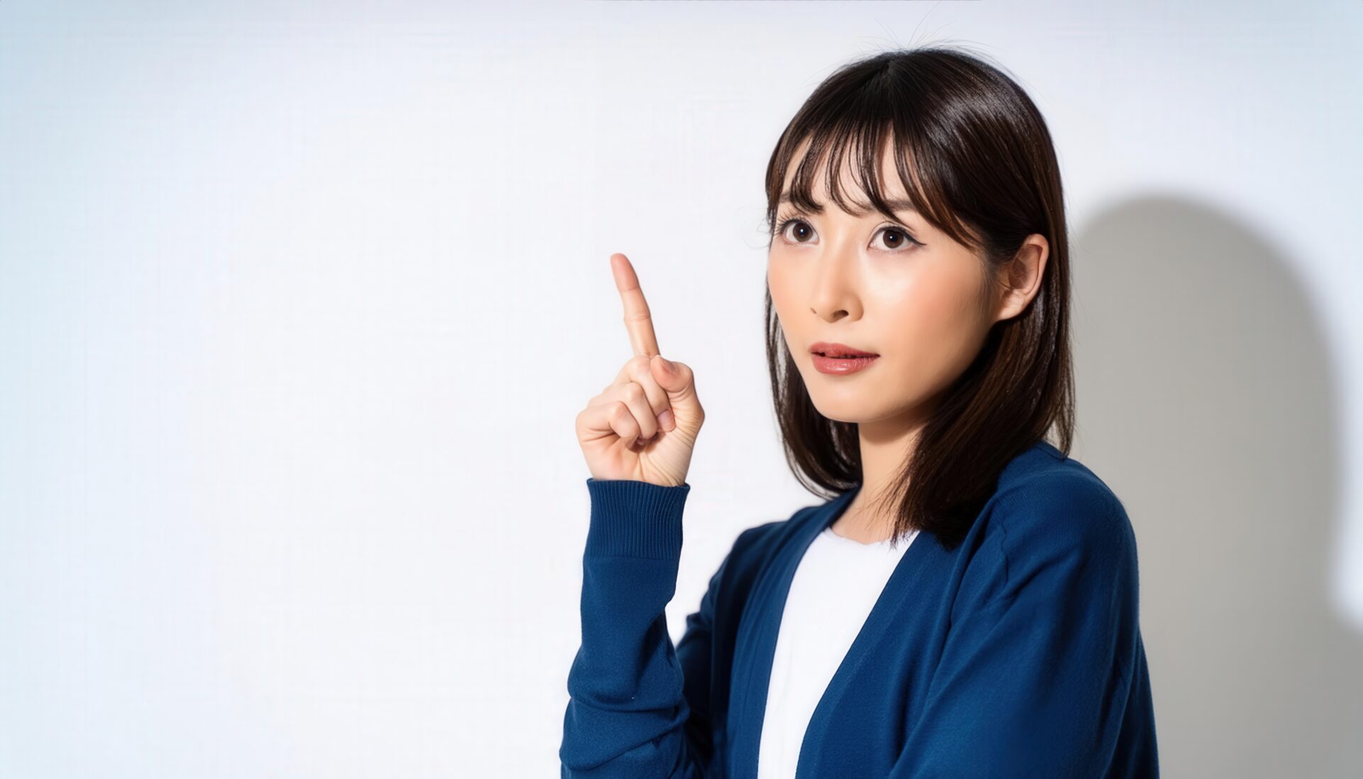 白背景で人差し指を立てる若い女性（ネイビーカーディガン）