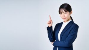 白背景で人差し指を立てる若い女性（ネイビースーツ）
