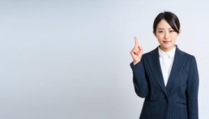 白背景で人差し指を立てる若い女性（ピンストライプスーツ）