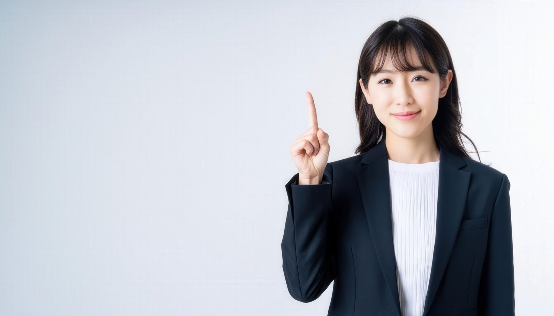 白背景で人差し指を立てる若い女性（ビジネススーツ）