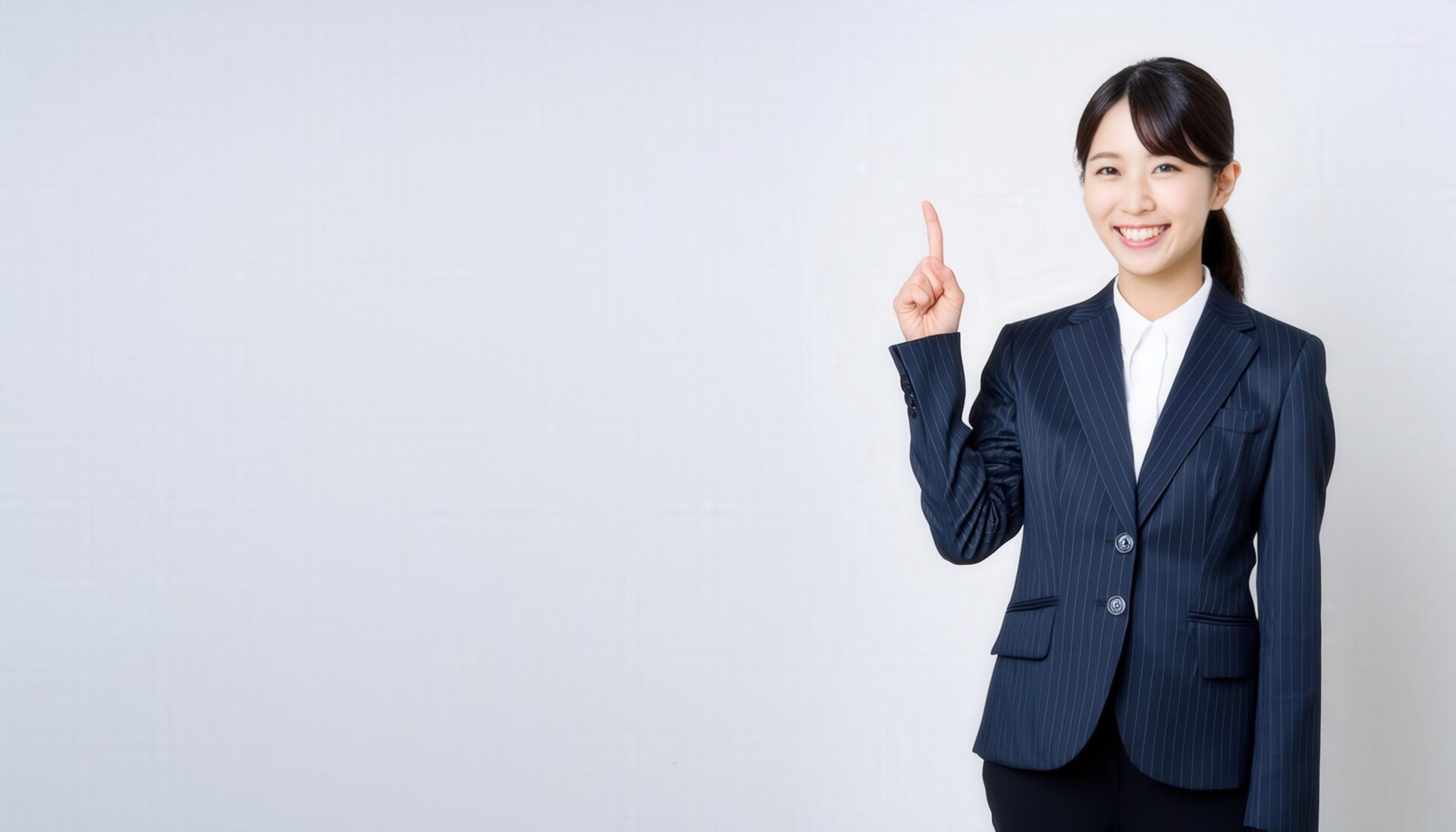 白背景で指差しポーズをとる若い女性（スーツ）