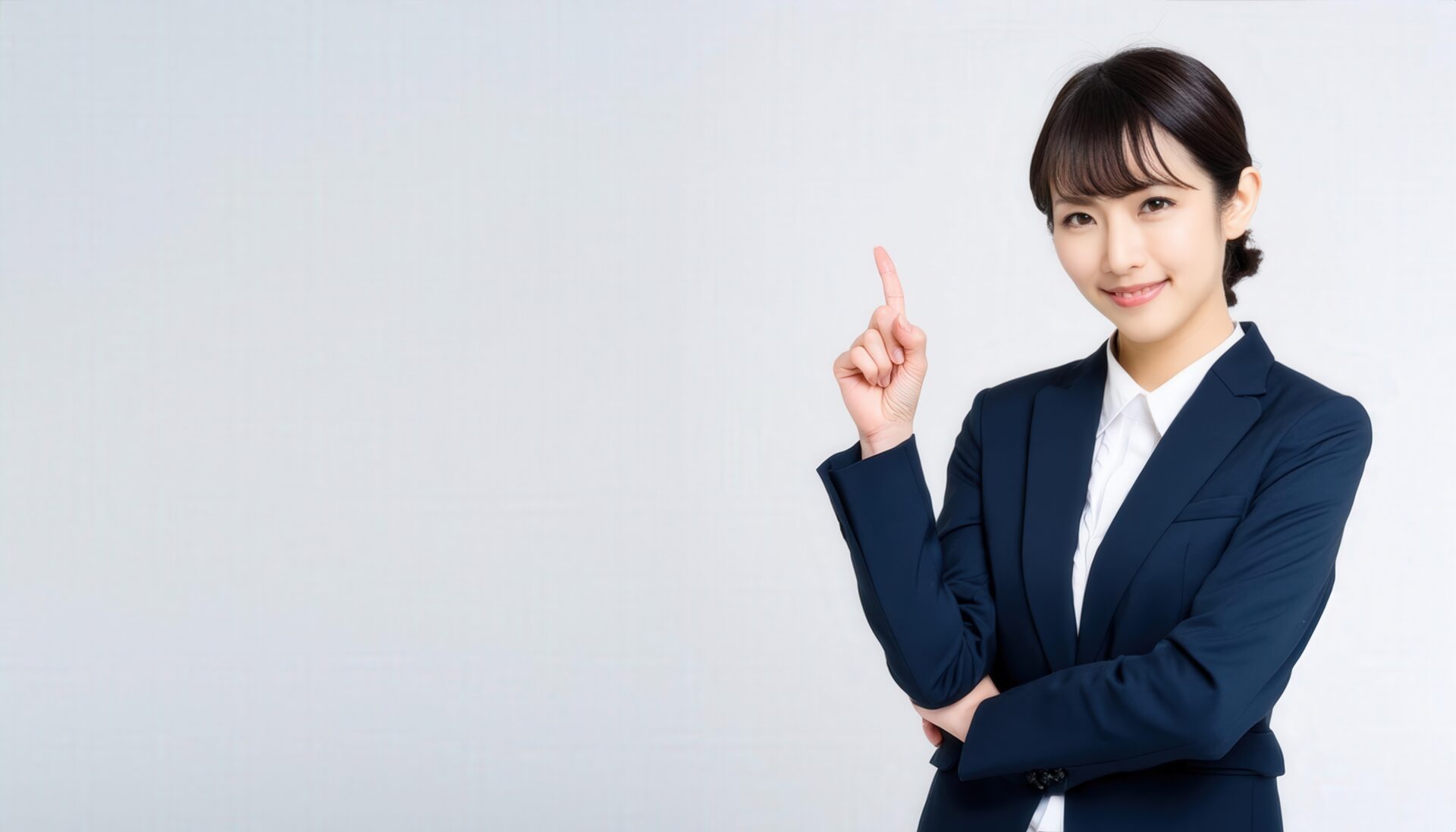 白背景でポイントジェスチャーをする若い女性（スーツ）