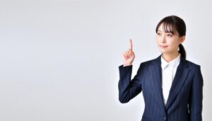 白背景で人差し指を立てる若い女性（スーツ）