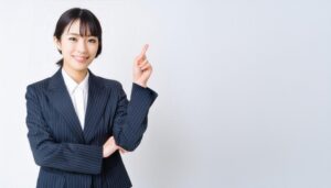 白背景で人差し指を立てる若い女性（ピンストライプスーツ）