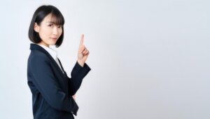 白背景で指差しをする若い女性（スーツ）