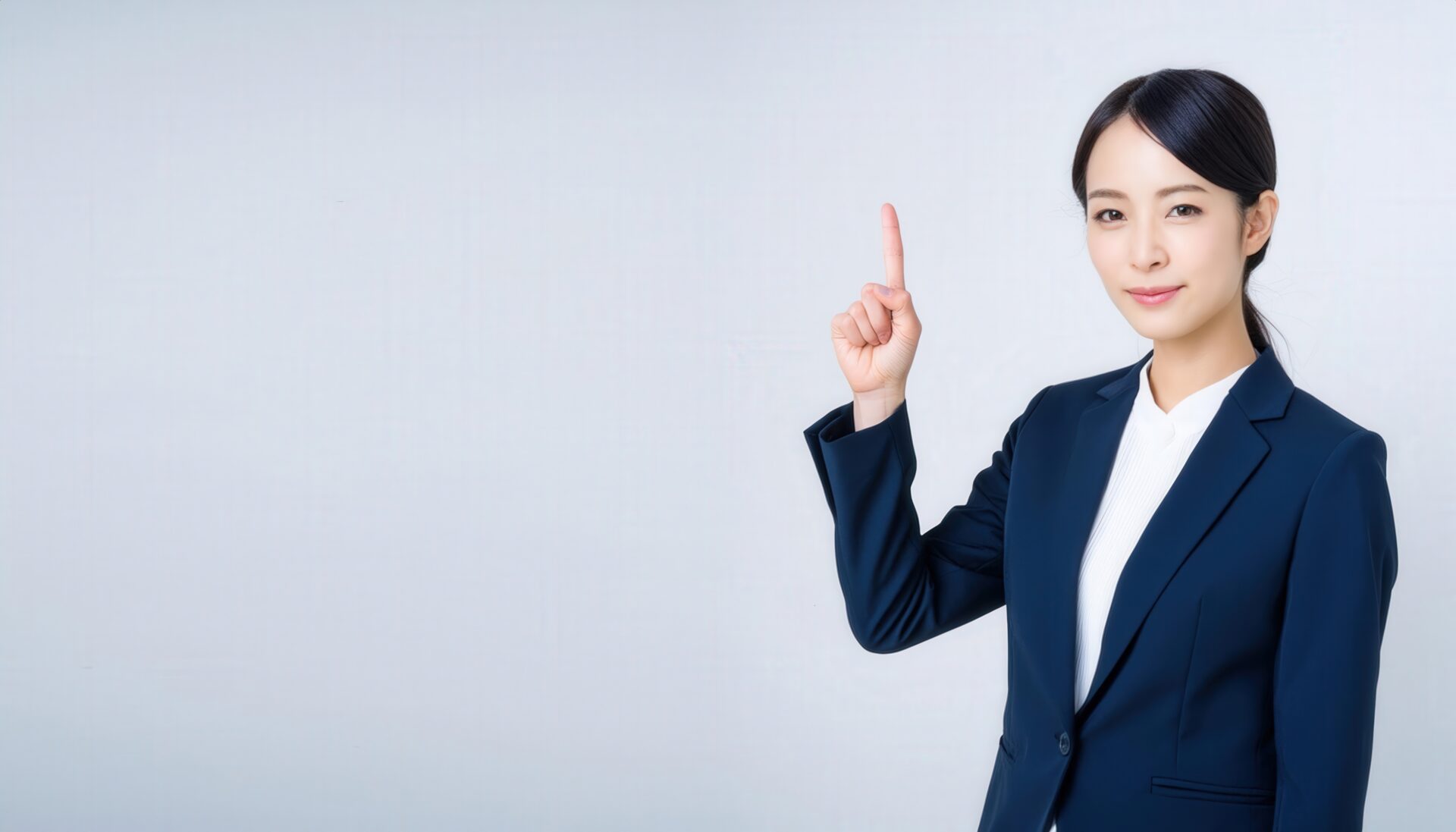 白背景でポイントのポーズをする若い女性（スーツ）