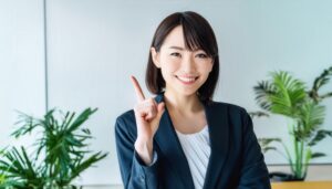 オフィスで人差し指を立てる若い女性（ビジネススーツ）