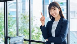 オフィスの窓辺で人差し指を立てる笑顔の若い女性