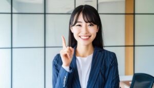 ガラスパーティションのあるオフィスで人差し指を立てる笑顔の若い女性