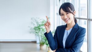 窓のあるオフィスで人差し指を立てる笑顔の若い女性