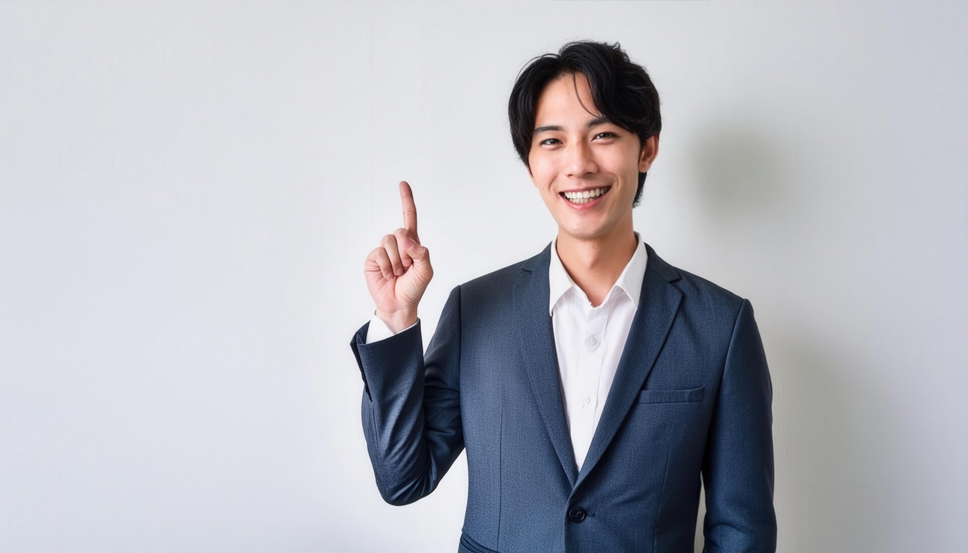 白背景でビジネススーツを着て人差し指を立てる笑顔の若い男性