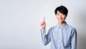 白背景でストライプシャツを着て人差し指を立てる笑顔の若い男性