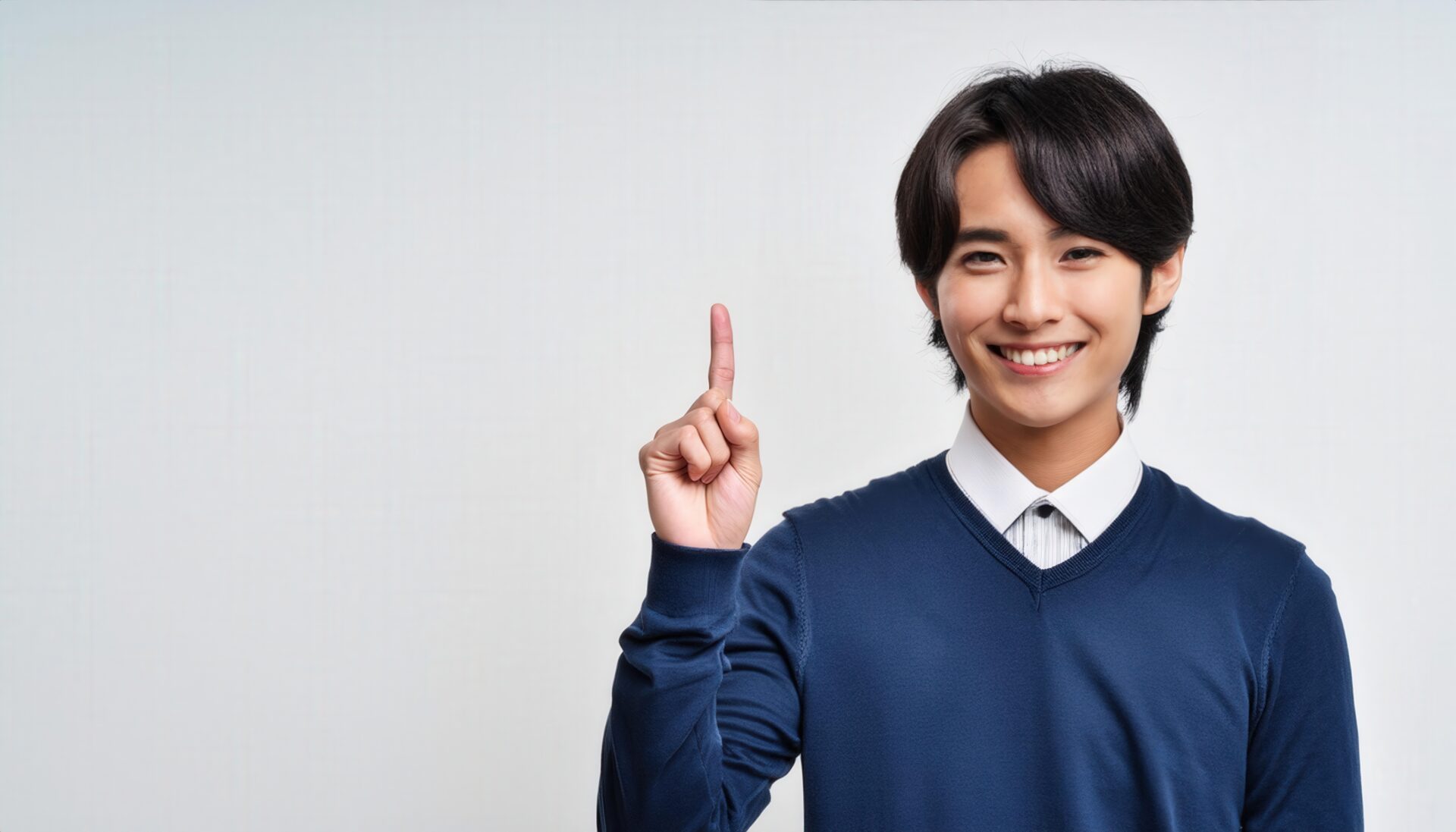 白背景で人差し指を立てる笑顔の若い男性（紺色のセーター）
