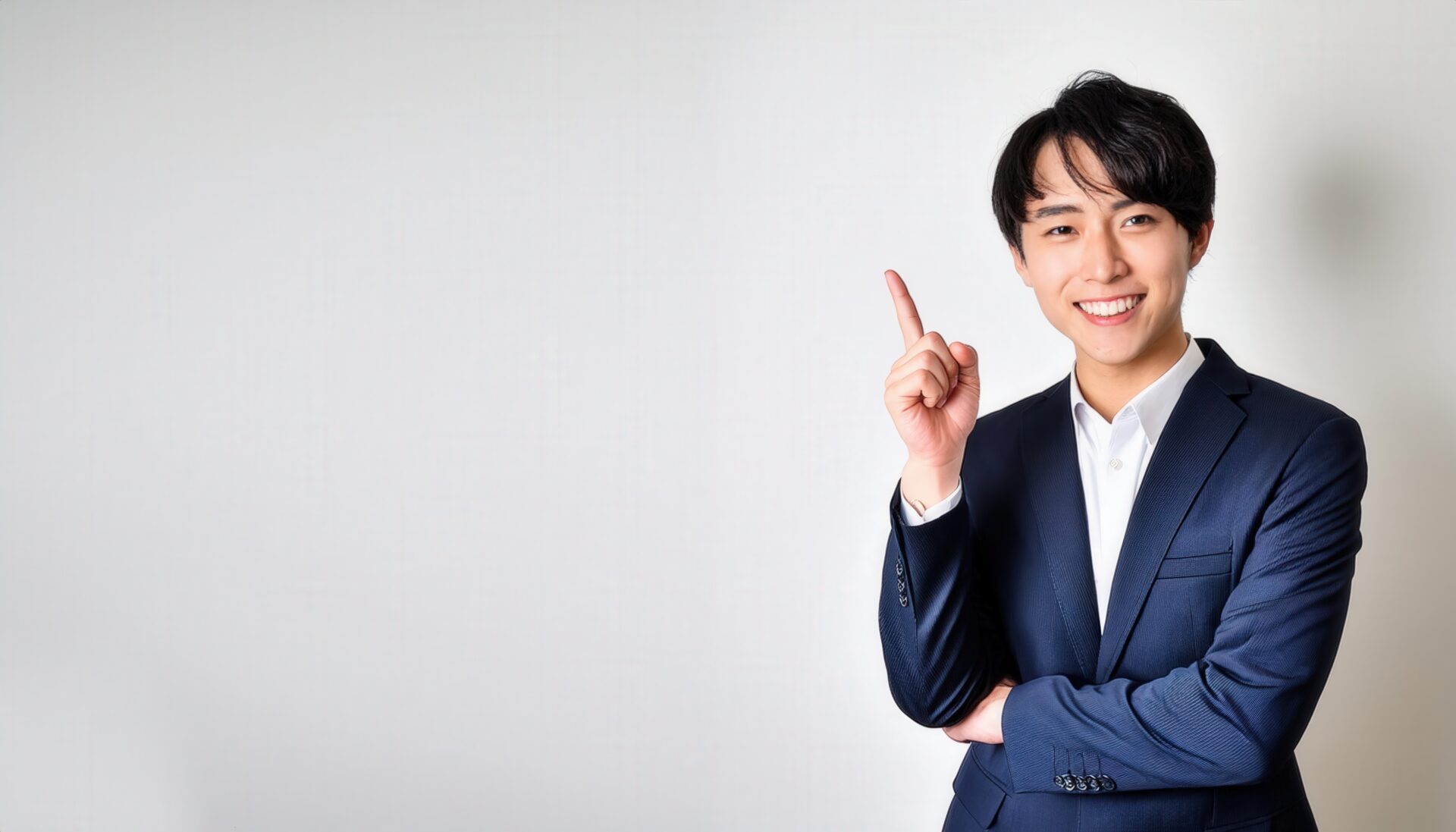 白背景で人差し指を立てる笑顔の若い男性（ビジネススーツ）
