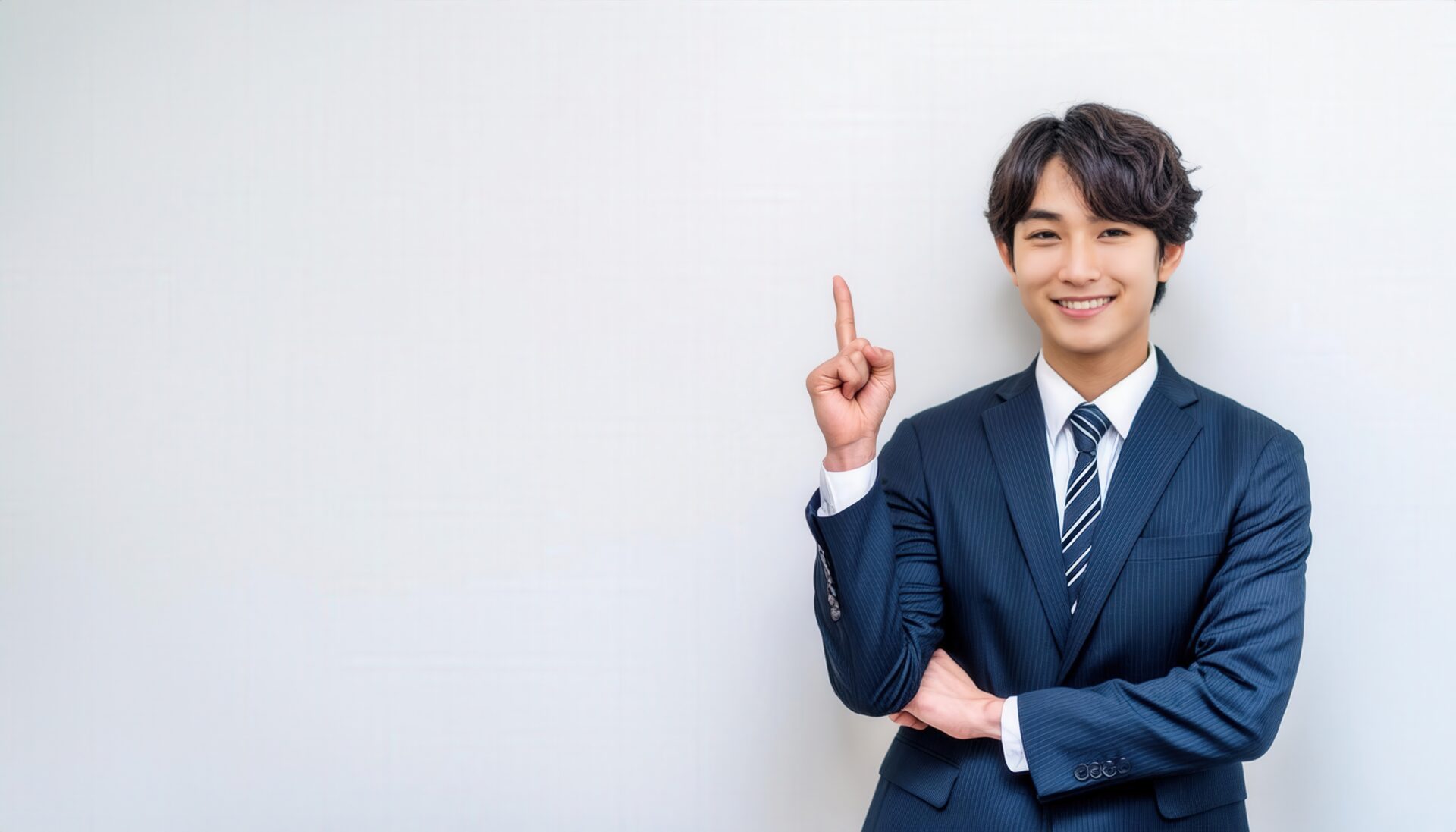 白背景で人差し指を立てる笑顔の若い男性（ストライプタイ）