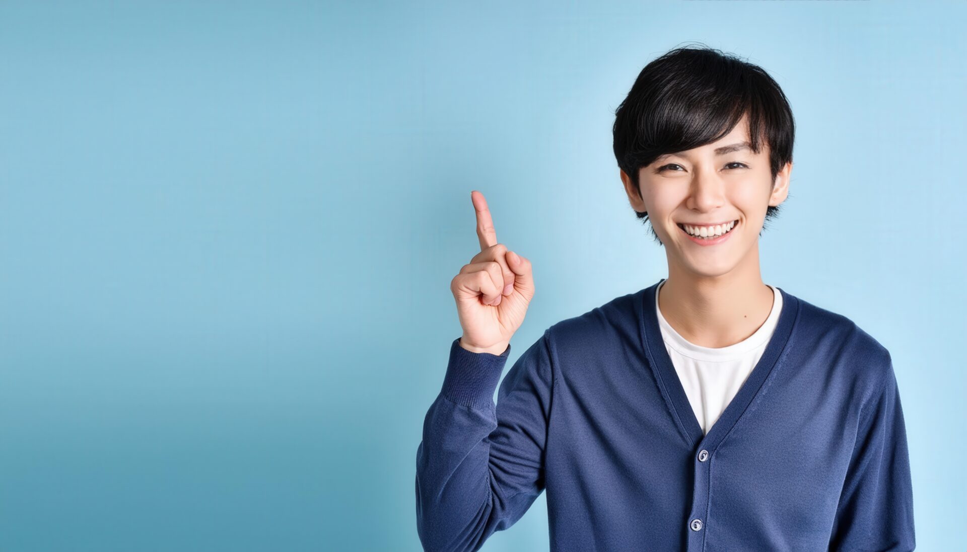 水色背景で人差し指を立てる笑顔の若い男性（ネイビーカーディガン）