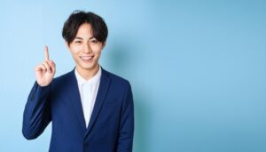 水色背景で人差し指を立てる笑顔の若い日本人男性