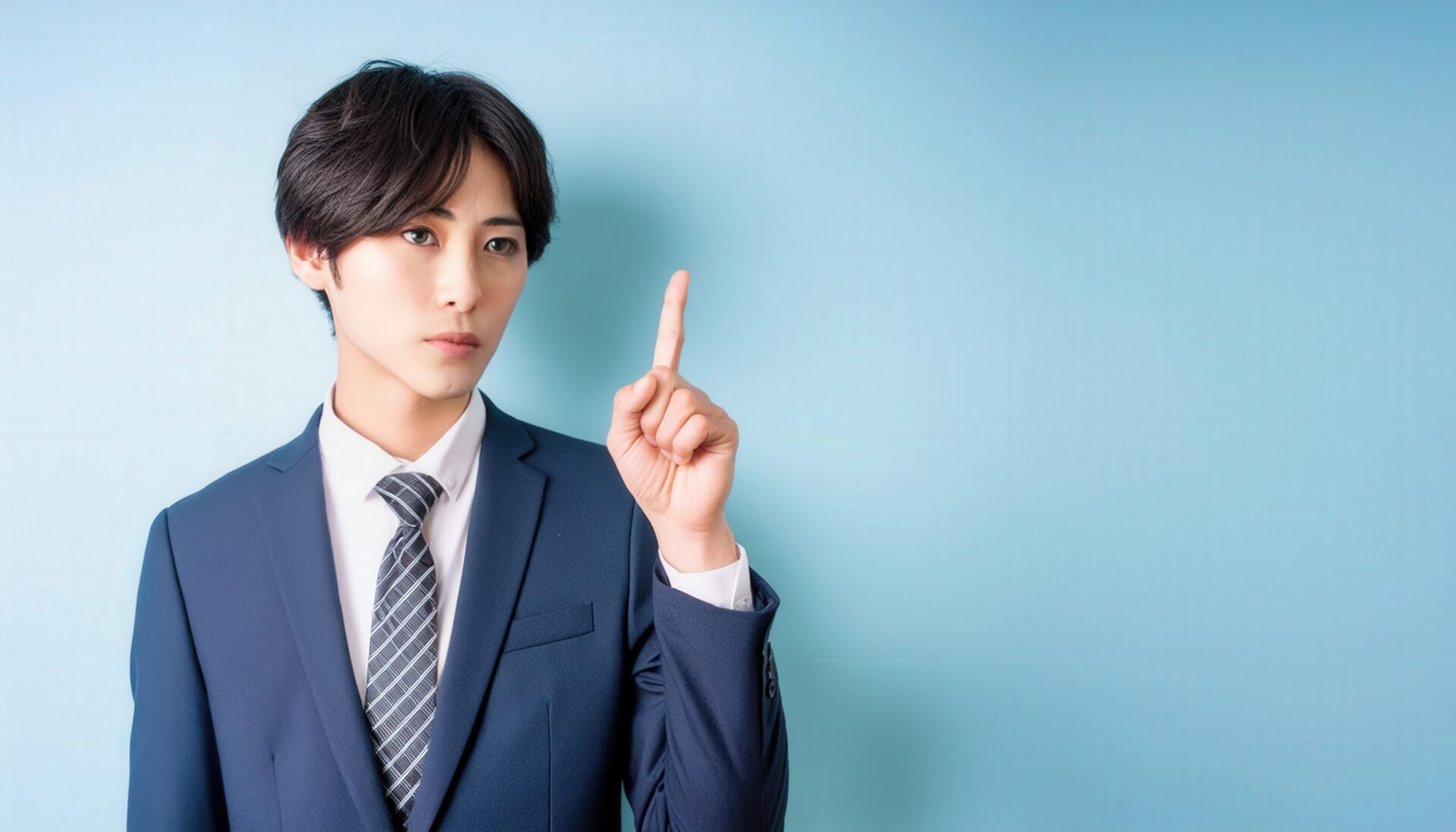 水色背景で人差し指を立てる若い男性（ネイビースーツ）