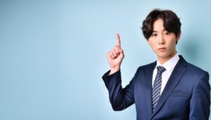 水色背景で人差し指を立てる若い男性（ストライプシャツ）