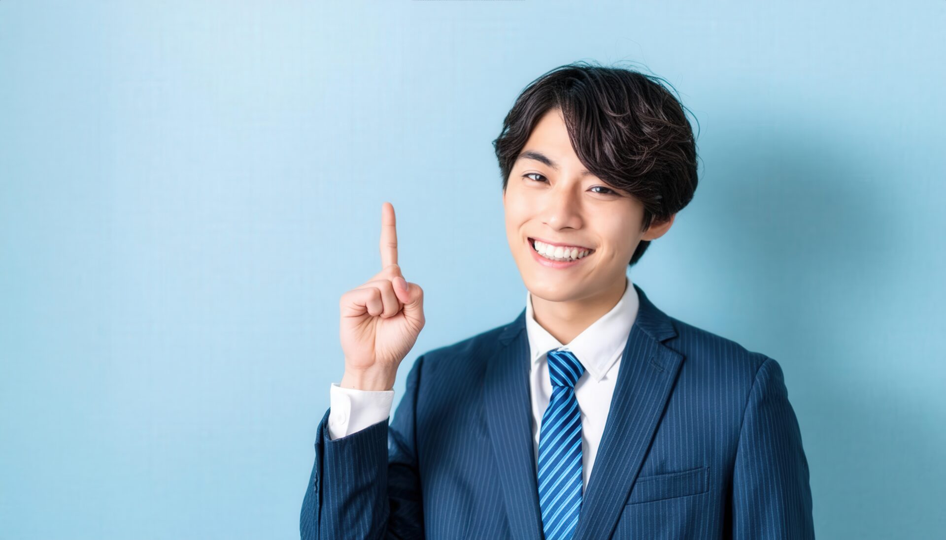 水色背景で人差し指を立てる若い男性（ストライプスーツとブルータイ）