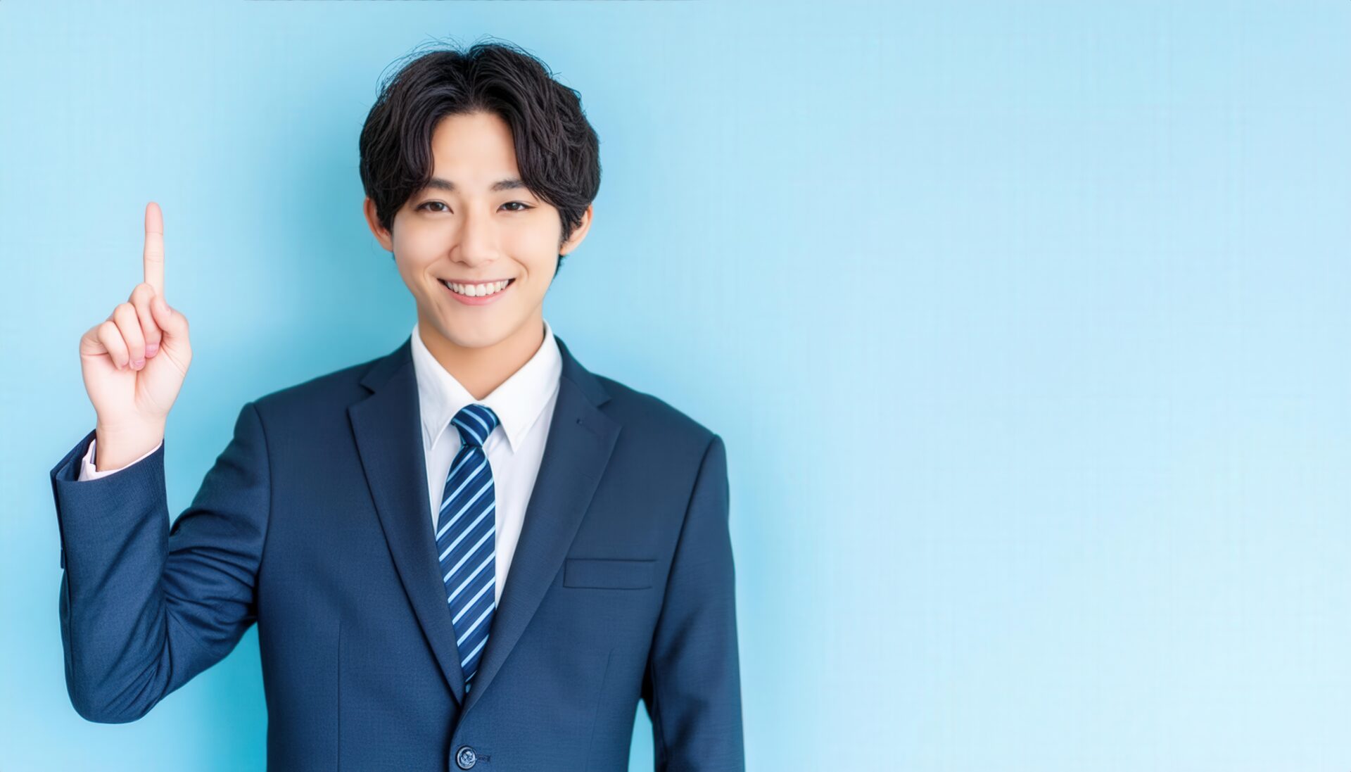 水色背景で人差し指を立てる若い男性（ネイビースーツとブルータイ）