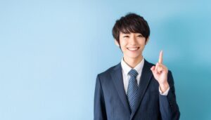 水色背景で人差し指を立てる若い男性（ストライプスーツとストライプタイ）
