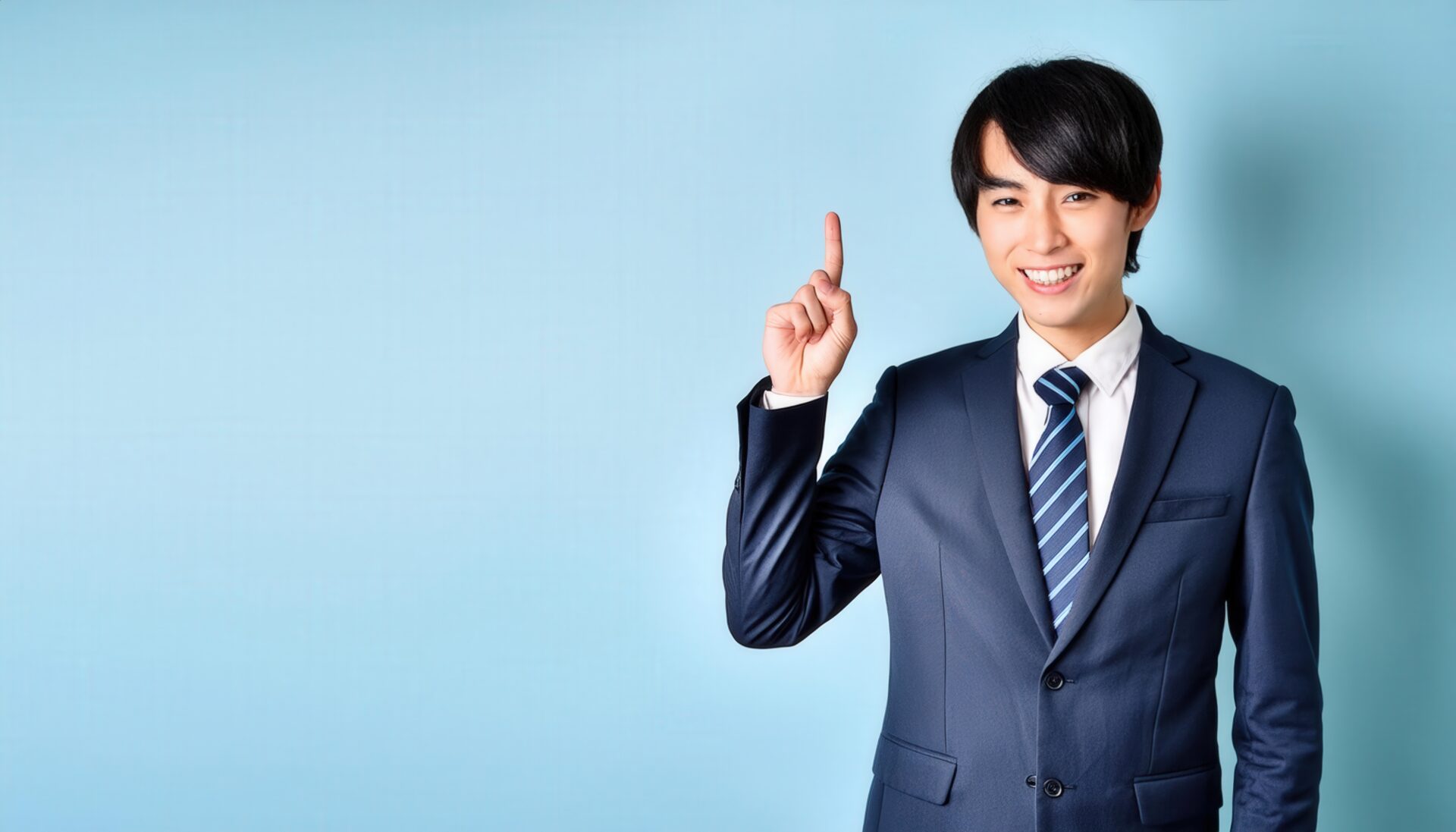 水色背景で人差し指を立てる若い男性（ネイビースーツと無地タイ）