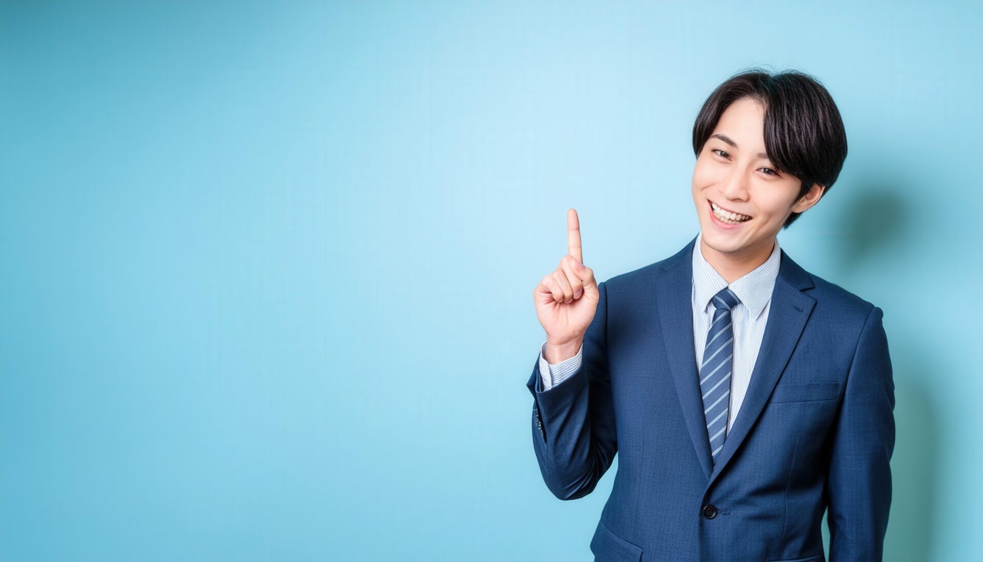 水色背景で人差し指を立てる若い男性（ネイビースーツとストライプタイ）
