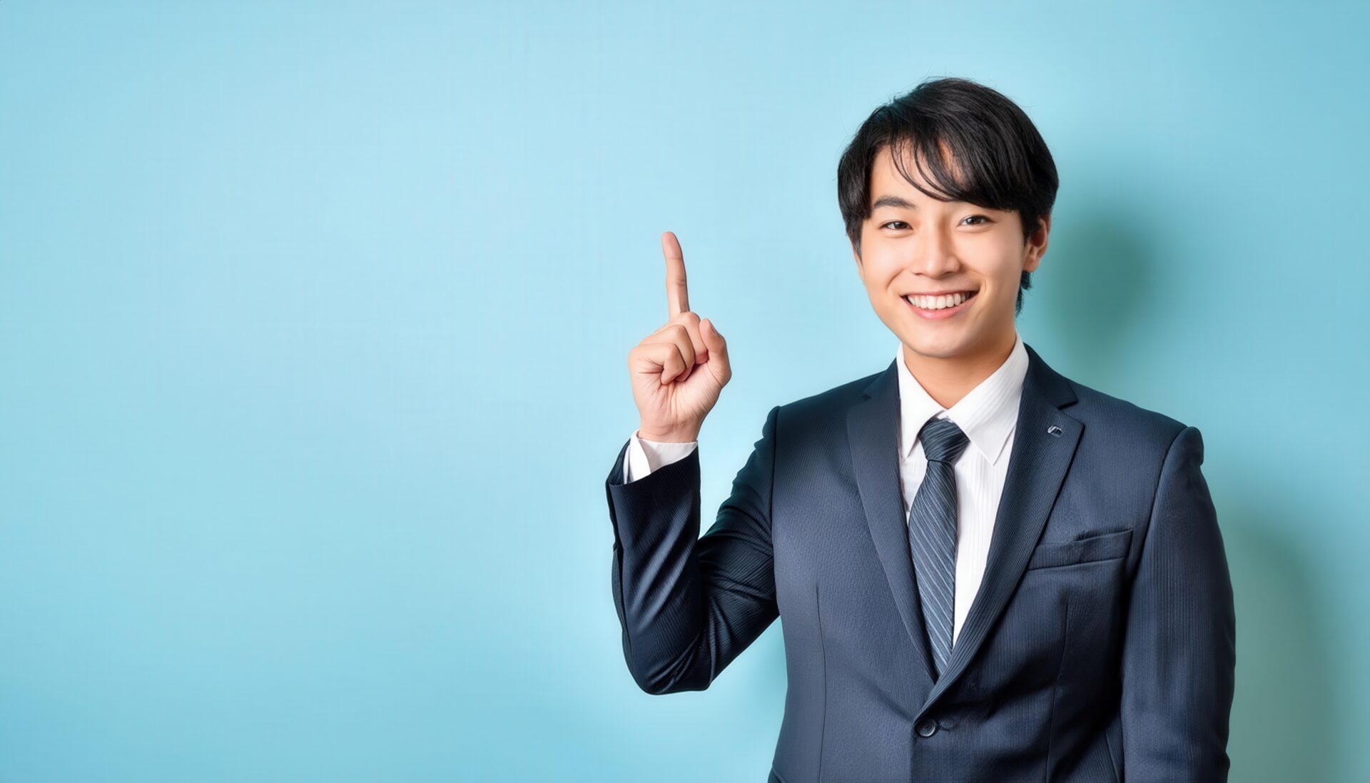 水色背景で人差し指を立てる笑顔の若い男性（スーツ・ダークネクタイ）