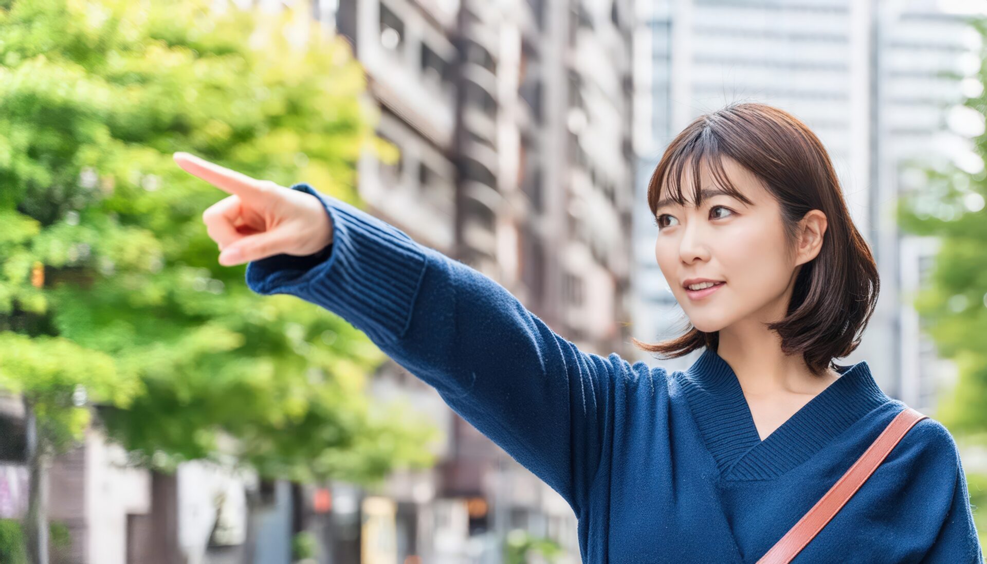 ネイビーのセーターを着た若い人が街中で指をさす