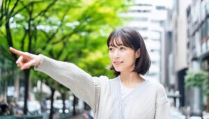 ホワイトのニットを着た若い人が街中で指をさす