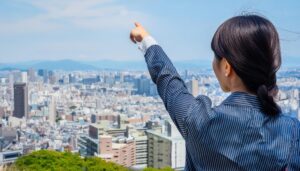 ストライプスーツを着た後ろ姿の若い人が高台から街を指す